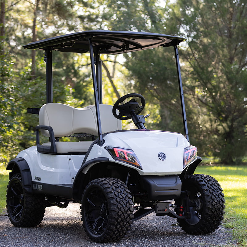 4" King XD Yamaha Drive2 lift kit installed on white cart parked on driveway with trees in the background and oversized wheels and tires with fender flares.