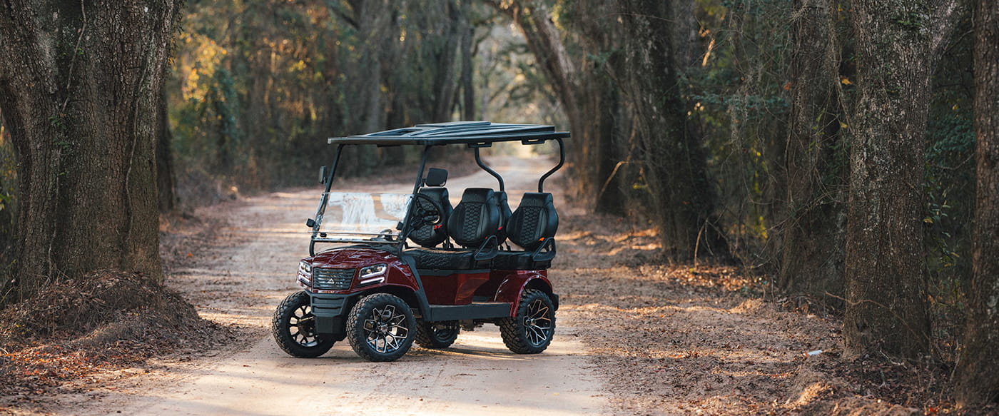 Brand new Sierra AX4 LSV in red metallic finish with premium black seats in 4-forward configuration, parked in driveway with a backdrop of trees.