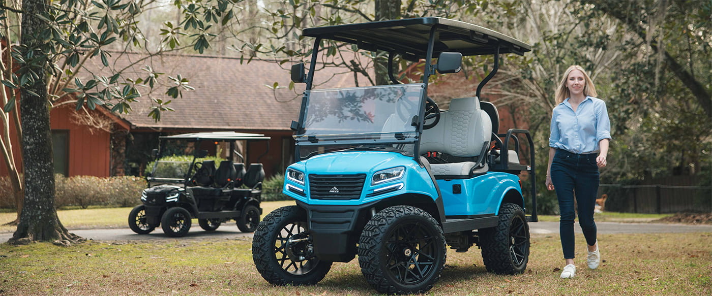 Sierra AX2 golf cart and personal transportation vehicle (PTV) with blue body and gray seats parked in a front yard, featuring folding windshield, all-terrain tires, street legal light kit, touchscreen display, and flip folding rear seat for 4 passengers.